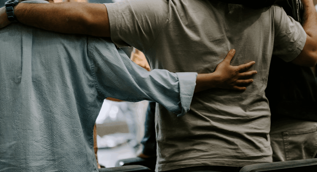 A support group of men embrace one another in a circle.