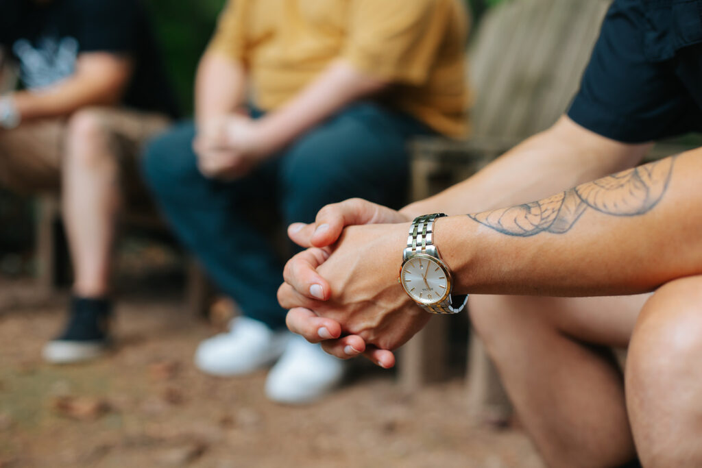 Men sit in a circle with their hands together in prayer