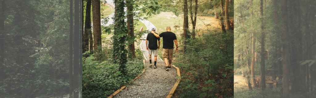 Two men support each other while walking along a path