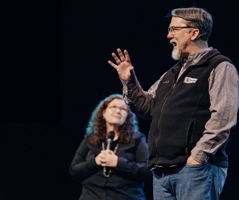 Man speaking on stage with woman holding microphone. Church event.