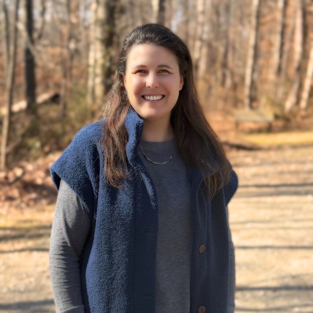 Smiling woman in a blue vest outdoors on a sunny day
